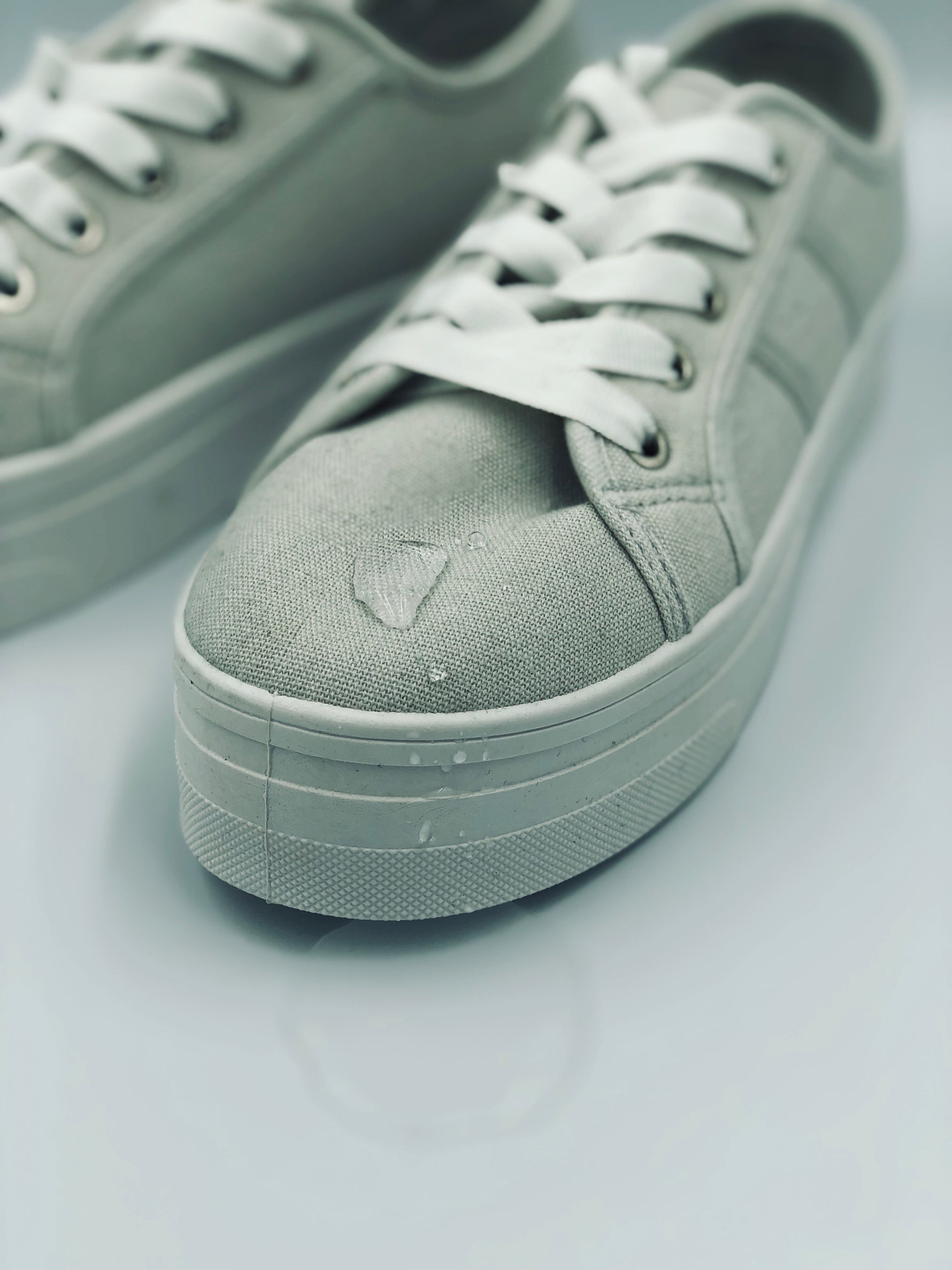 Pair of gray sneakers with white laces with water repelling from its surface