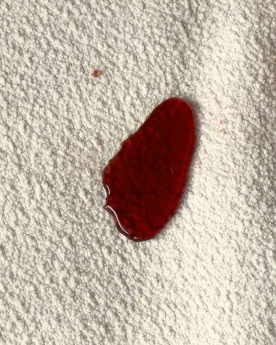 A translucent deep red liquid spill, from wine, beading on a textured bouclé fabric. This demonstrates the "after" effect of protectME on fabric, showing the spill protection.
