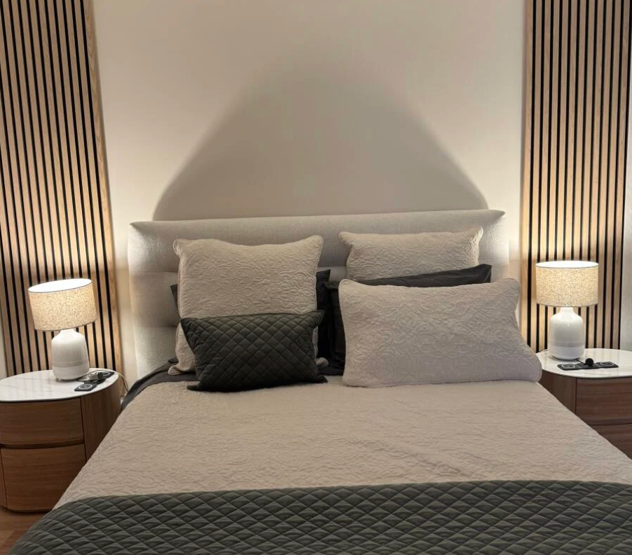 Neatly made bed with pillows in a bedroom setting with side tables and lamps.